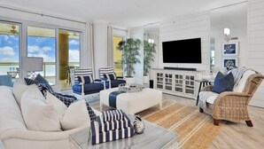 A spacious living room with a large flat-screen TV, comfortable seating, and a view of the outdoors.