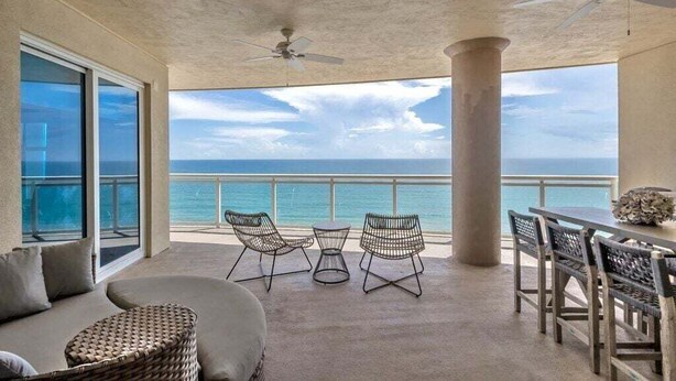 A balcony with a view of the ocean, furnished with a sofa, chairs, and a table.