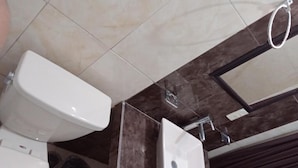A bathroom with a toilet, sink, and shower area. - Hotel Kiko (Mazatlán)