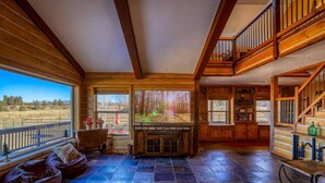 A spacious living area with a large window overlooking a scenic landscape, a fireplace, and a cozy seating area. - Stunning Views, Foosball, Outdoor Fireplace, 30 Min to Wolf Creek Ski Resort! (Pagosa Springs)