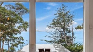 Une pièce avec vue sur la mer et les arbres, une table avec un bol de collations, et deux petits objets posés sur la table.