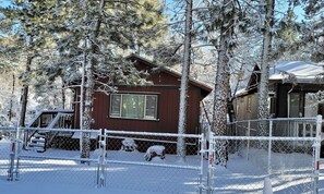 Eine Hütte mit roter Fassade, umgeben von schneebedeckten Bäumen und einem eingezäunten Garten.