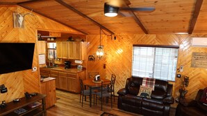 L’intérieur d’un chalet en bois comprend un coin repas, un canapé en cuir et un téléviseur.