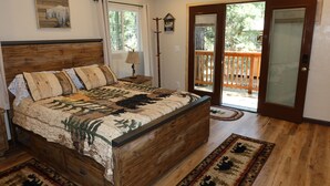 Une chambre à coucher avec un lit en bois, une table de chevet, une lampe, une fenêtre et une porte-fenêtre donnant sur un balcon.