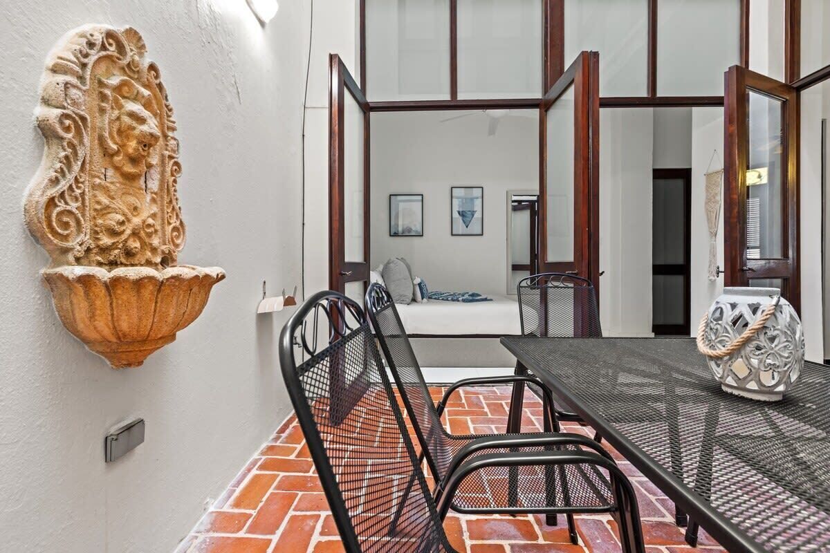 Zona pranzo con pavimento in mattoni, sedie in metallo, un tavolo e un elemento decorativo a parete.