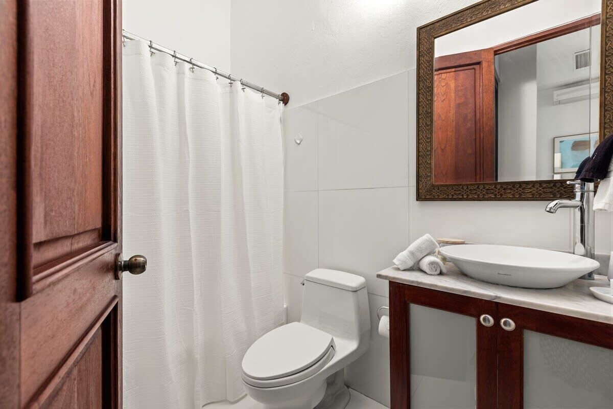 A bathroom with a white toilet, a wooden cabinet with a mirror above the sink, and a shower curtain.