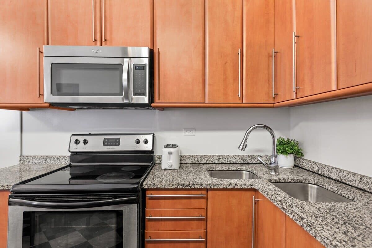 A kitchen with wooden cabinets, a stainless steel microwave, a stove, a toaster, and a sink.