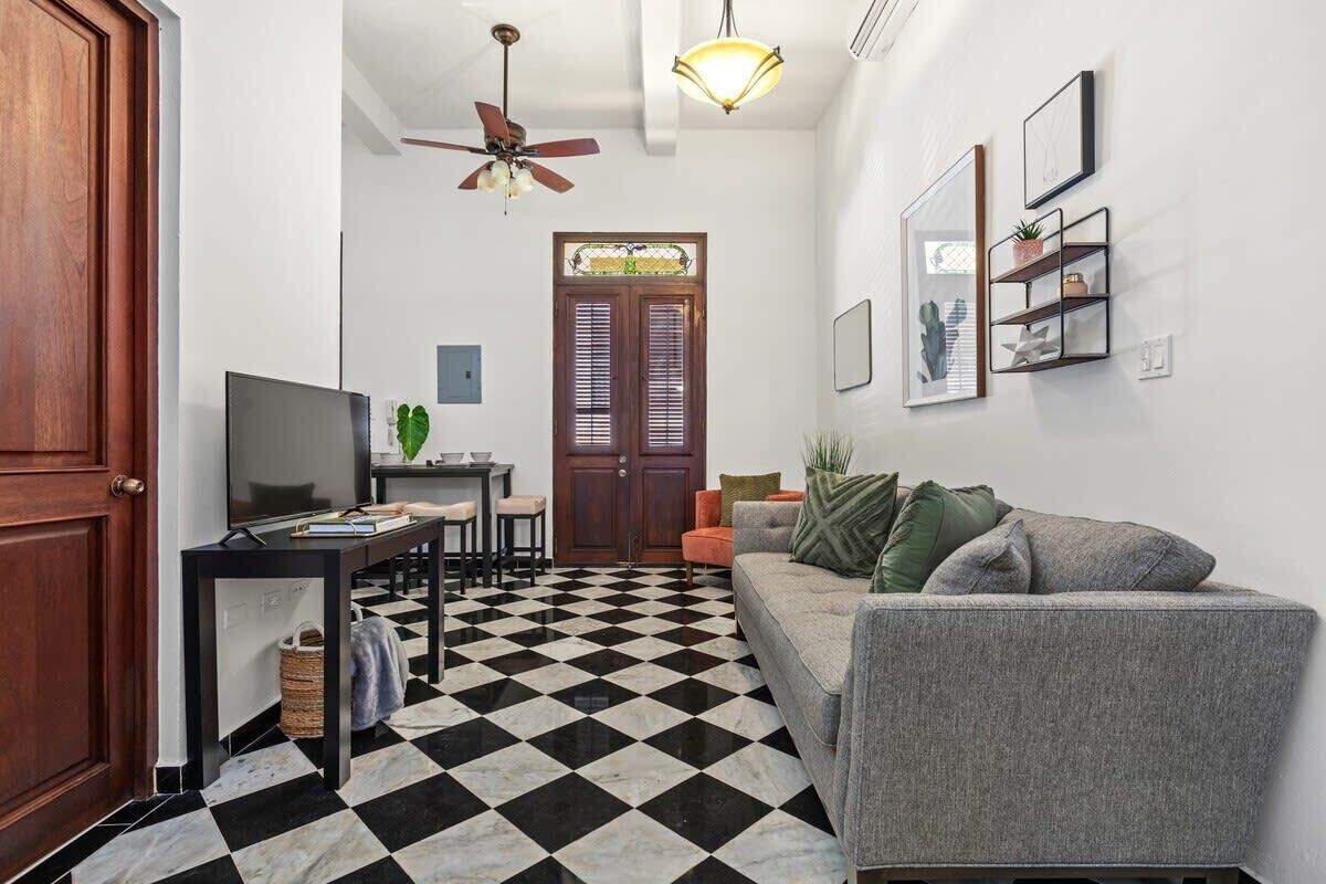 Un salon avec un sol à carreaux, un canapé, un téléviseur, un ventilateur de plafond et une porte à panneaux de verre.