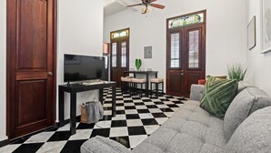 Ein Wohnzimmer mit schwarz-weiß kariertem Boden, einem grauen Sofa, einem Fernseher, einem Deckenventilator und einem Essbereich mit Tisch und Stühlen.