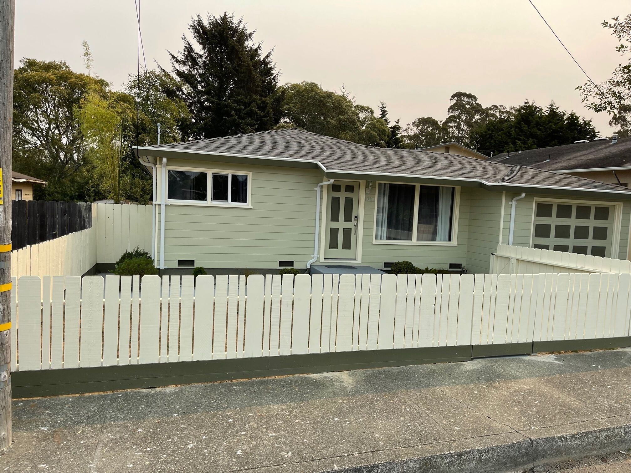 Une maison de plain-pied avec une clôture en bois peinte en blanc, une porte d’entrée et un garage.
