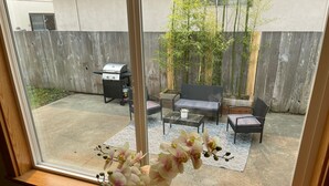 Un patio con una parrilla, mobiliario exterior y una planta de bambú.