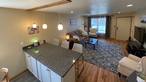 Una sala de estar moderna con área de cocina, que incluye una mesa de comedor, sofá y televisor.