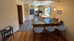 Una cocina moderna con una isla central, taburetes de bar y un comedor con ventana al jardín.