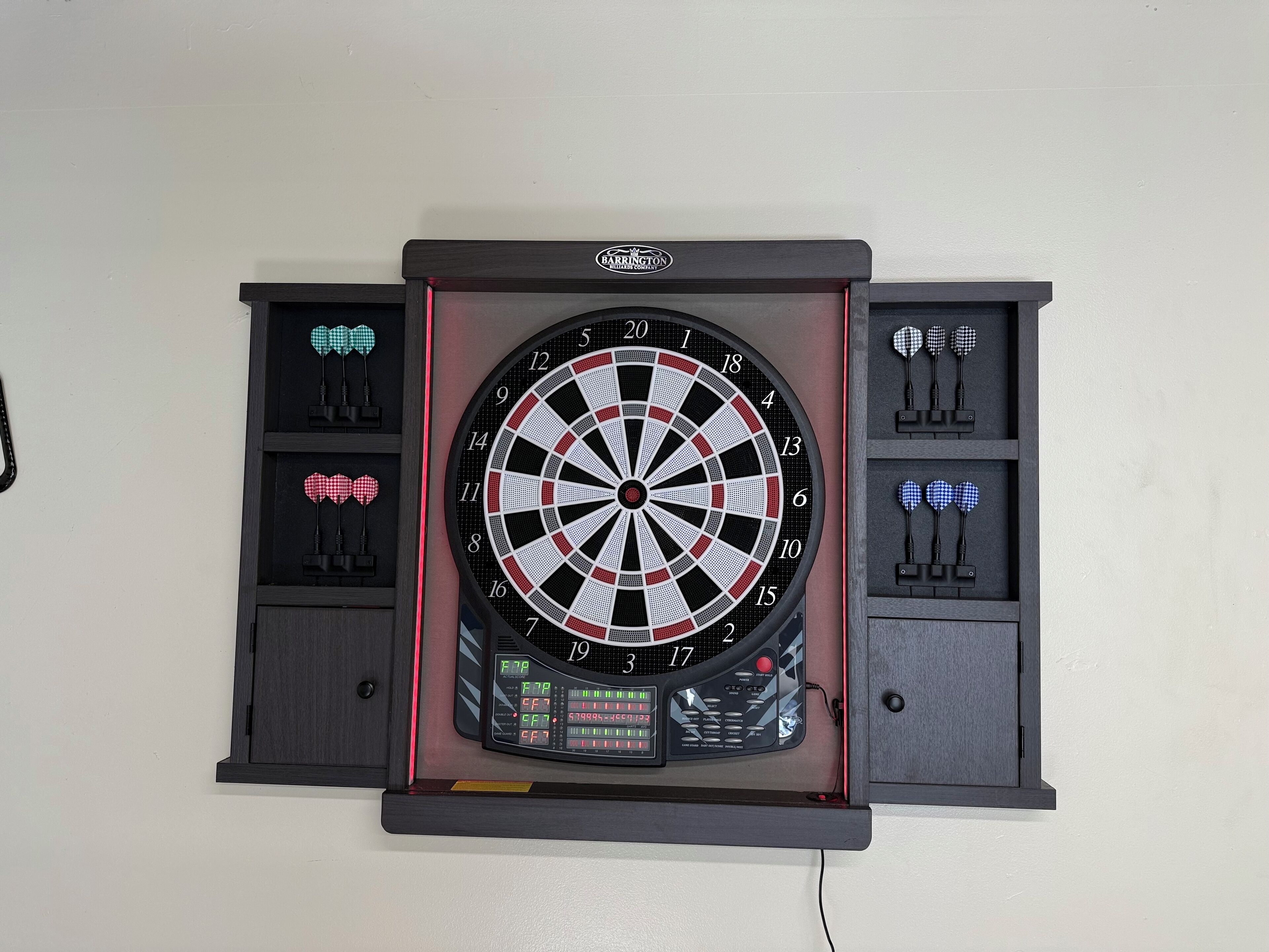A dartboard mounted on a wall with a digital score display and a dart case holder.