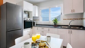 Una cocina moderna con un refrigerador de acero inoxidable, horno empotrado, lavamanos y comedor con mesa lista para el desayuno.