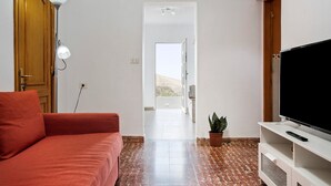 Una sala de estar con un sofá, un televisor sobre un mueble, una lámpara y una planta en maceta.