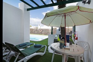 Une terrasse avec deux chaises longues, une table et un parasol à rayures.