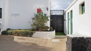 Valkoinen rakennus, jonka sisäänkäynti on portilla, pieni puutarha-alue ja kyltti, jossa lukee: »Apartamentos Las Palmeras 111».
