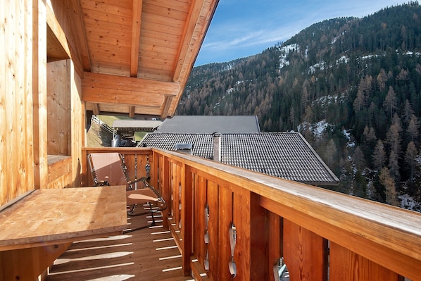 A wooden balcony with a table and chairs, overlooking a mountainous landscape.
