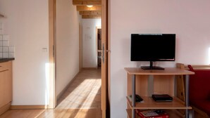 Una habitación con un televisor sobre un soporte de madera, una puerta que da a otra habitación y un suelo de baldosas.