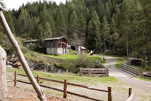 A rustic cabin with a stone foundation, surrounded by a wooden fence and a dirt path leading to a wooden bridge.