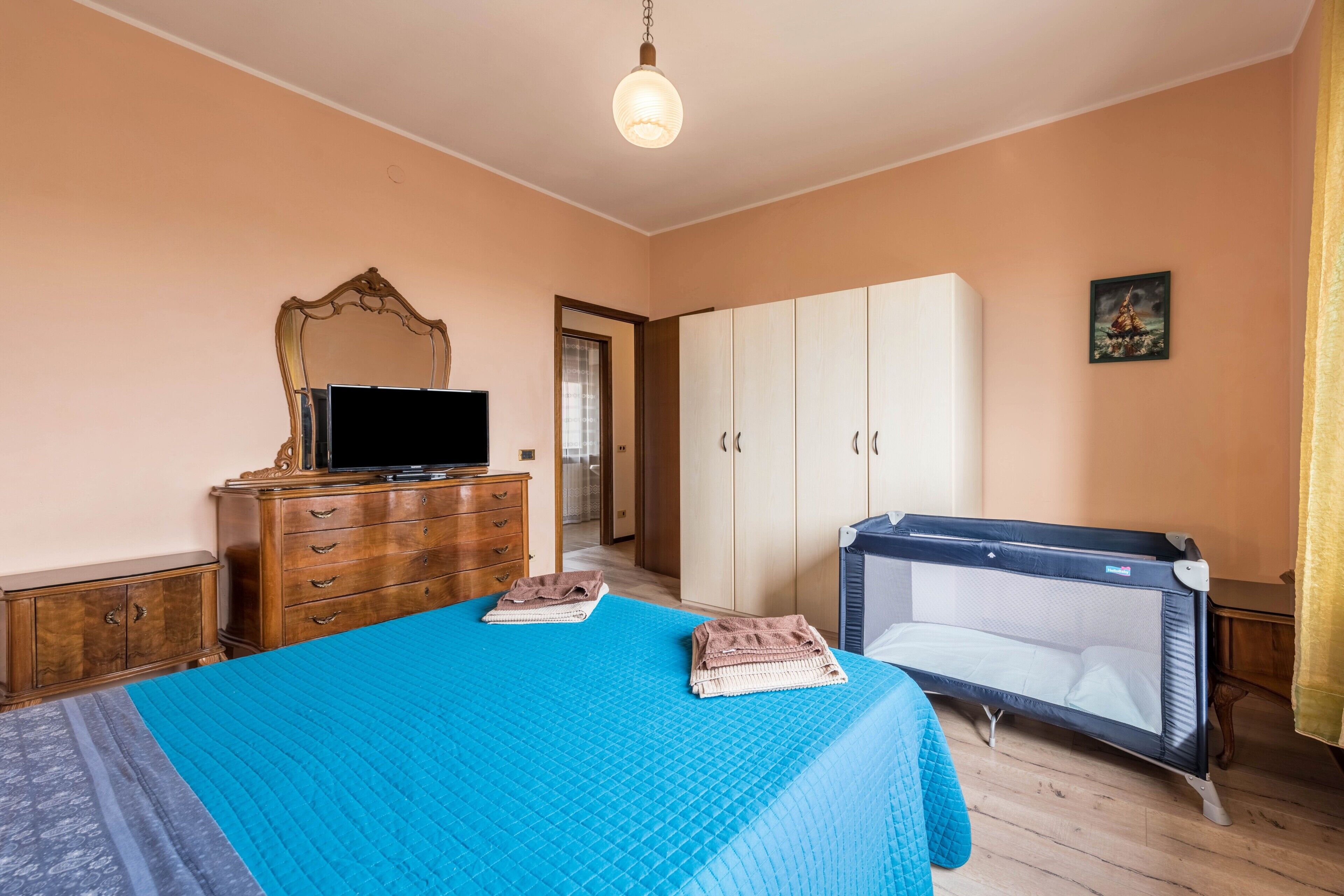 Una camera da letto con un letto, una cassettiera, una televisione, una culla e un armadio.