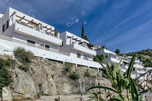 Un bâtiment situé sur la côte, doté de nombreux balcons, de murs extérieurs blancs et surplombant une colline rocheuse.