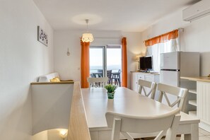 Une cuisine moderne avec des meubles blancs, une table à manger avec des chaises, un téléviseur et un réfrigérateur.