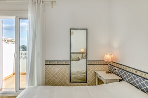 Une chambre à coucher avec un lit, une table de chevet avec une lampe, un miroir et une vue sur le balcon extérieur.