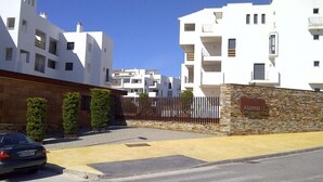 Un quartier résidentiel avec des immeubles modernes aux façades blanches, un mur de pierre sur lequel est apposée une plaque, et une voiture garée.