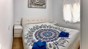 A bedroom with a bed, a nightstand, a wall-mounted artwork, and a window with curtains.