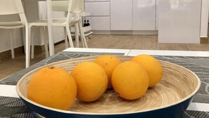 A dining table with a bowl of oranges and a coffee maker in the background.