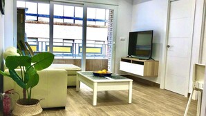 A living room with a sofa, a coffee table with fruit, a TV, and a balcony with a view.