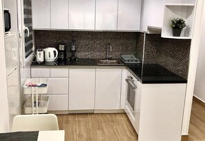 A compact kitchen with white cabinets, a black countertop, a tiled backsplash, and a small window with a plant. - Apartment 'Beach   Jolanta' with Sea View, Wi-Fi and Air Conditioning (Torrevieja)
