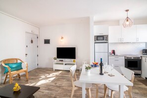 A modern kitchen with white cabinets, a microwave, and a stove. There is a dining table with chairs and a TV in the background.