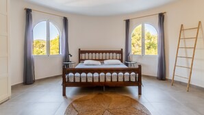 A bedroom with a wooden bed, two bedside tables, a round rug, and large windows with curtains. - Fantastic villa - Great location with Sea View, Pool & Wi-Fi (Moraira)