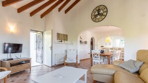 A living room with a TV, white coffee table, beige sofa, and a clock on the wall. - Fantastic villa - Great location with Sea View, Pool & Wi-Fi (Moraira)