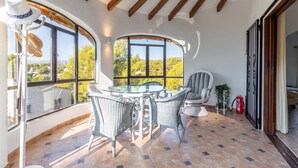 A sunlit patio with a glass table and wicker chairs, large windows with a view, and a fire extinguisher. - Fantastic villa - Great location with Sea View, Pool & Wi-Fi (Moraira)