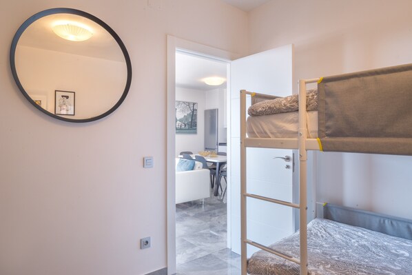 A bunk bed with a ladder, a round mirror, and a door leading to a dining area.