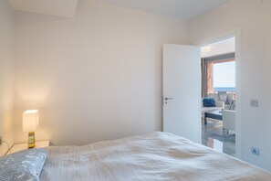 A bedroom with a bed, a nightstand, a lamp, and a door leading to a balcony with a view.