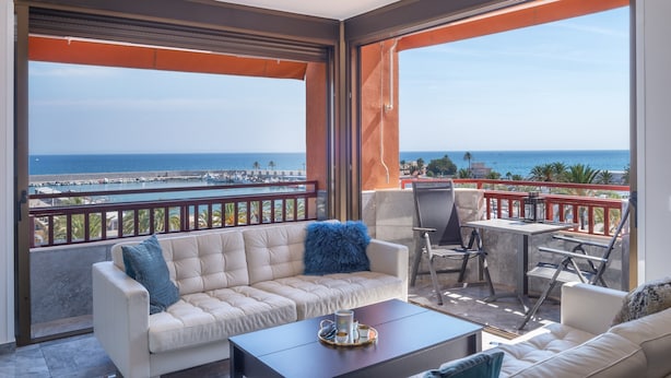 A balcony with a sofa, a table, and a chair, overlooking a coastal view. - "Marina view two bedroom apartment" with Sea View, Pool, Terrace & Wi-Fi (Fuengirola)