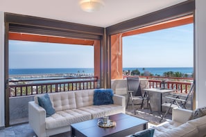 A balcony with a sofa, a table, and a chair, overlooking a coastal view.