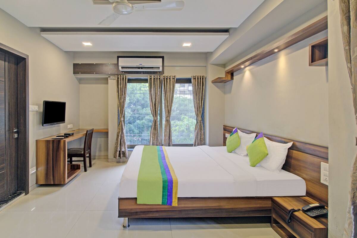 A hotel room with a bed, a desk, a TV, and an air conditioning unit.