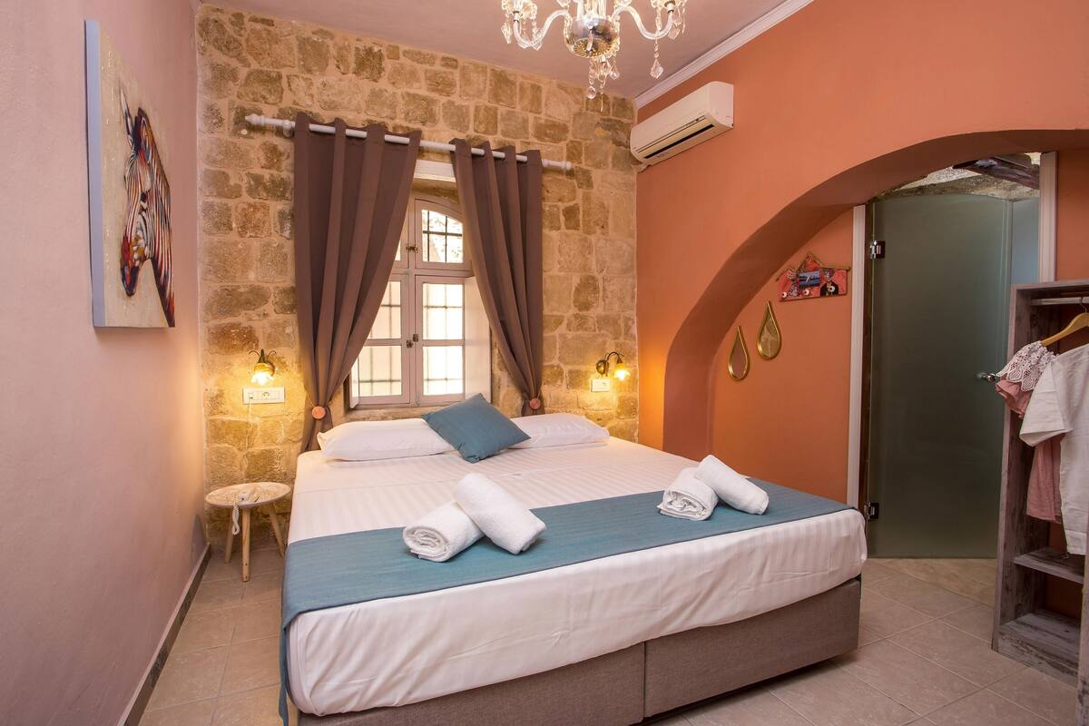 A bedroom with a stone wall, a bed with white linens, a blue throw, and a small round table.