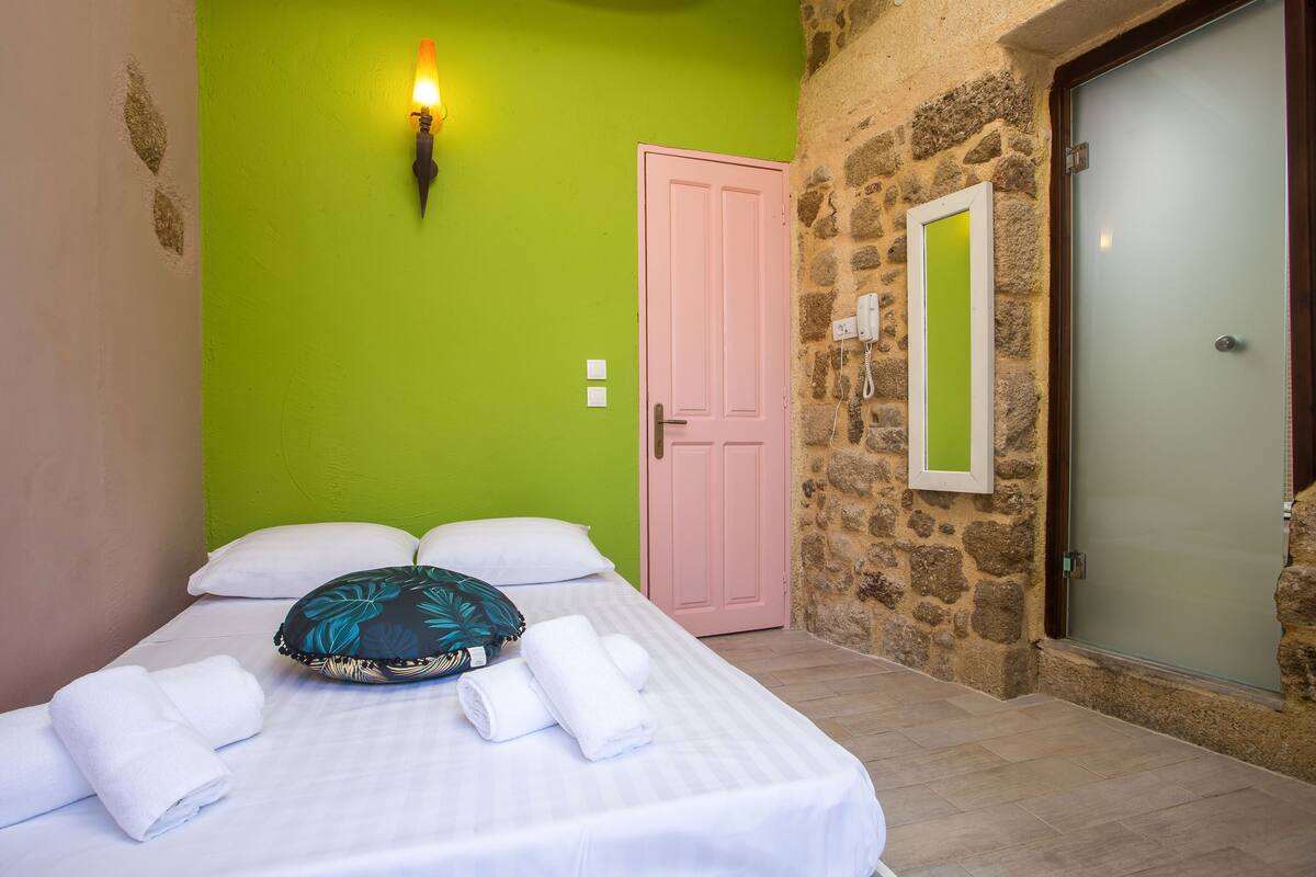 A room with a bed, a green wall, a pink door, and a stone wall.