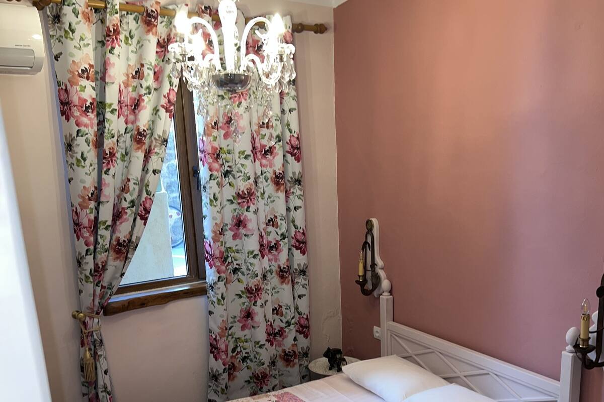 A neatly made bed with floral bedding, a bedside table with a lamp, and a window with floral curtains.