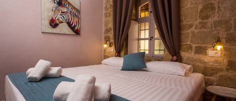 A neatly made bed with towels, a zebra painting, stone walls, and a small table.