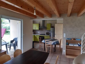 A kitchen with wooden beams, a dining area with a table and chairs, and a view through a glass door.