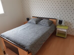 Een bed met een bedsprei met patroon, twee nachtkastjes, een nachtkastje met een speaker, en een behang met patroon.