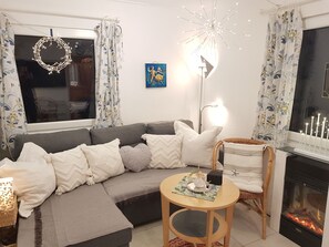 A cozy living room with a sectional sofa, a round wooden table, a fireplace, and a decorative light fixture.